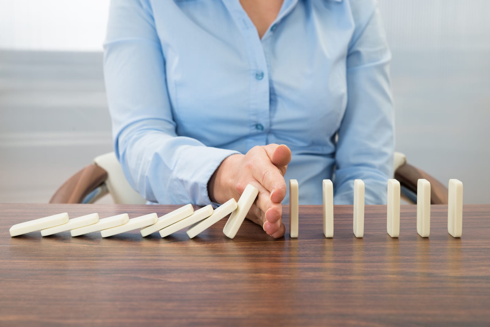 Exilis | A photo of a businesswoman stopping dominoes from falling