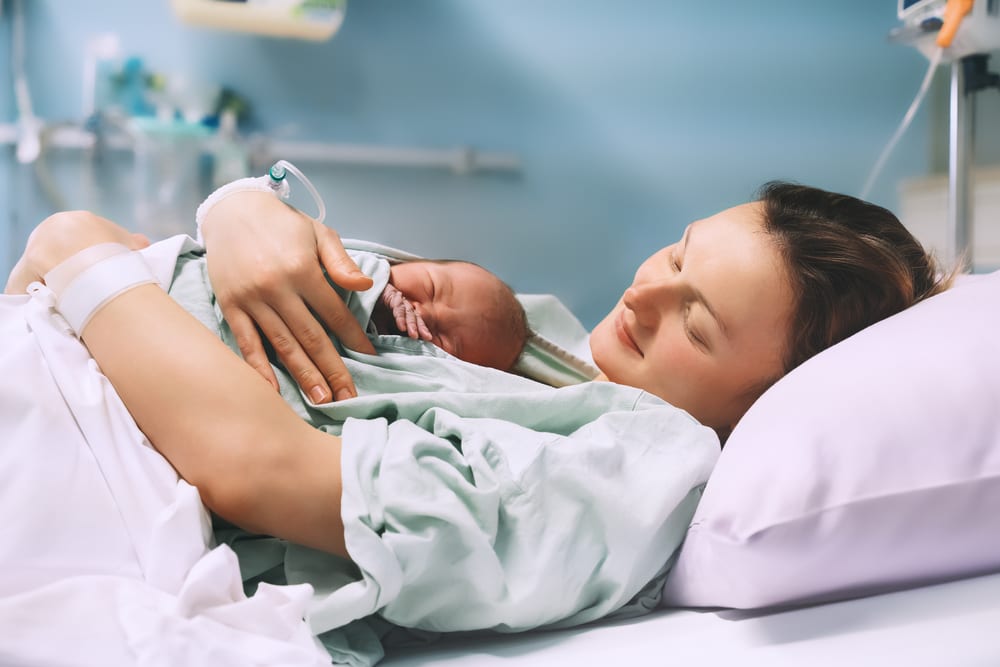 FemiLift | A woman with her baby in a hospital bed after giving birth.