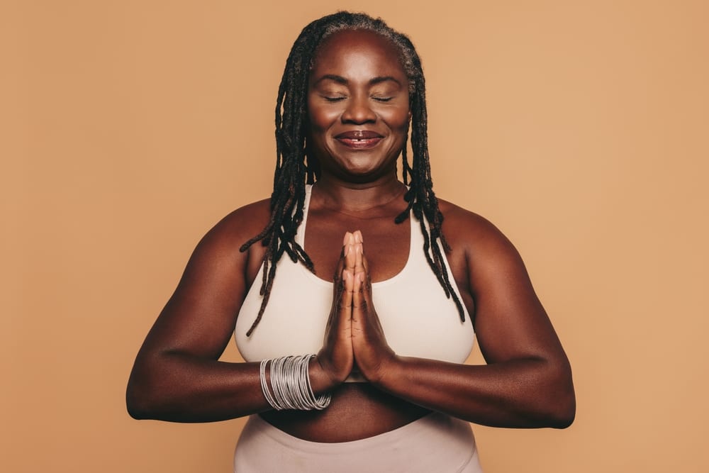 FemiLift | A mature black woman in activewear meditating with palms together.